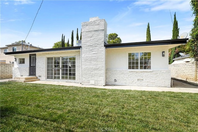 rear view of house featuring a lawn, fence, a chimney, and stucco siding