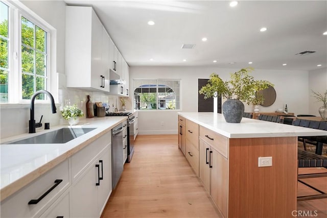 kitchen featuring a sink, a kitchen breakfast bar, range with gas stovetop, under cabinet range hood, and visible vents