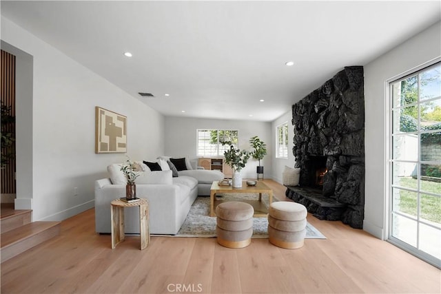 living area with light wood-style floors, a stone fireplace, recessed lighting, visible vents, and stairway