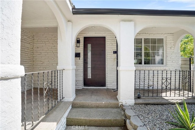doorway to property with brick siding and covered porch