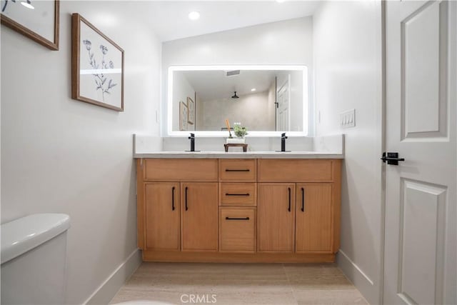 full bath with baseboards, double vanity, a sink, and toilet