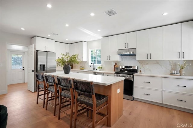 kitchen featuring a kitchen bar, visible vents, appliances with stainless steel finishes, light wood-type flooring, and under cabinet range hood