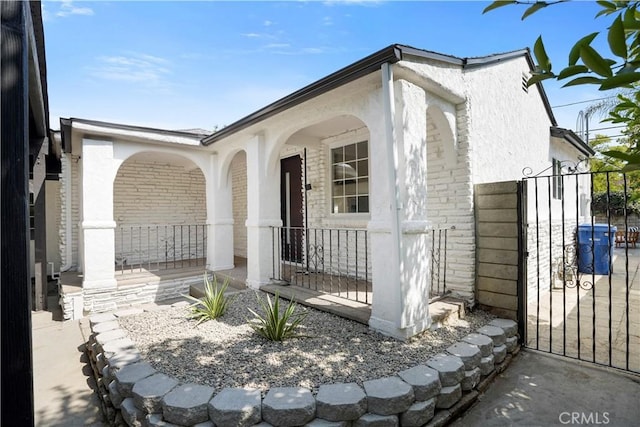 exterior space with a porch, brick siding, a gate, and stucco siding
