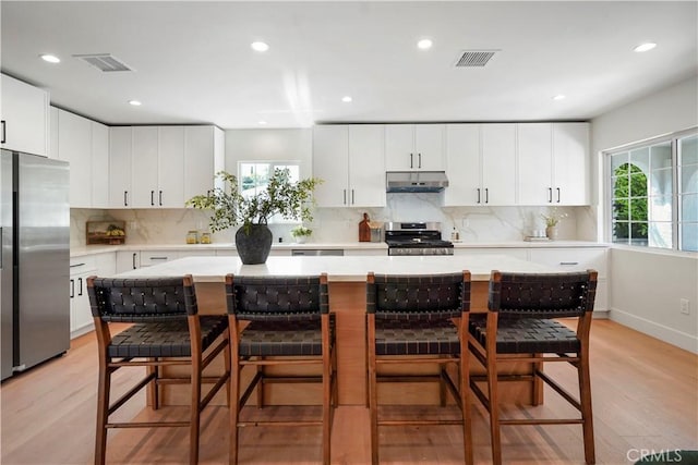 kitchen featuring visible vents, light wood-type flooring, light countertops, under cabinet range hood, and stainless steel appliances