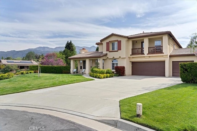 view of front of property featuring a tile roof, a garage, a front yard, concrete driveway, and a balcony