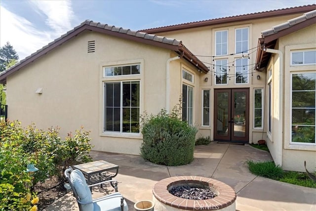 back of property featuring french doors, stucco siding, a fire pit, and a patio area