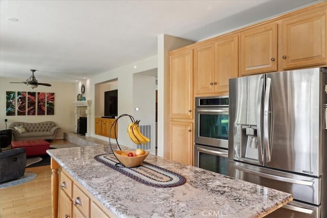 kitchen featuring light brown cabinetry, ceiling fan, light wood-type flooring, light stone counters, and stainless steel appliances