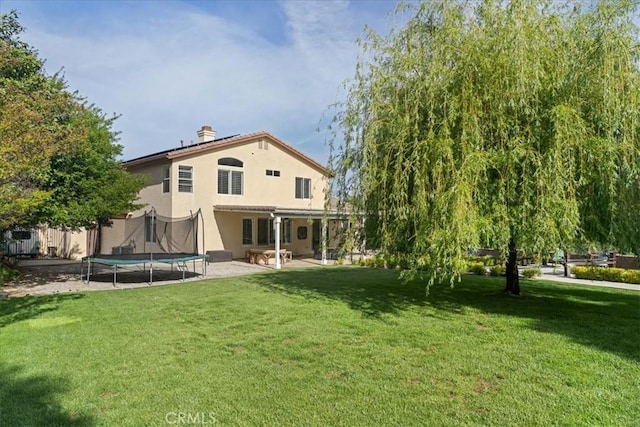 back of property featuring a trampoline, a patio area, stucco siding, and a yard