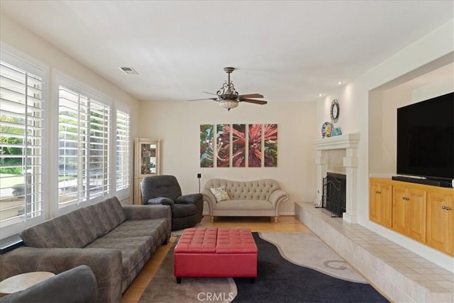 living room featuring a ceiling fan, visible vents, a fireplace with raised hearth, and wood finished floors