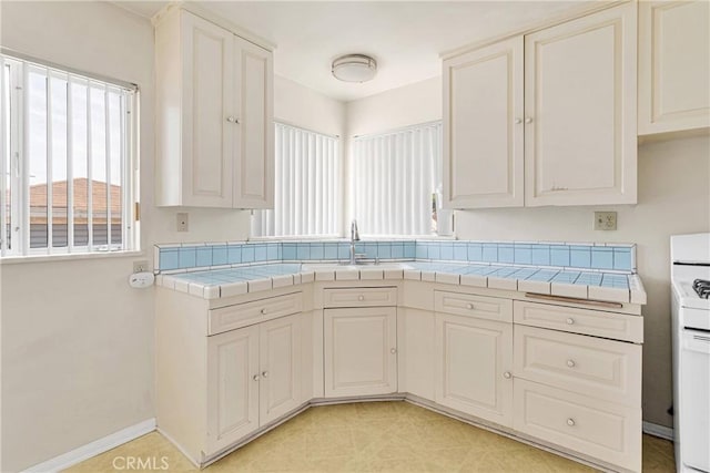 kitchen with a sink, baseboards, tile counters, and white range with gas cooktop