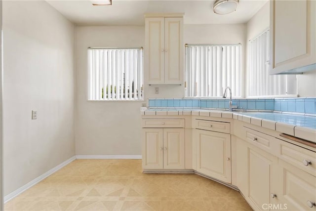 kitchen with baseboards, a sink, tile countertops, and cream cabinetry