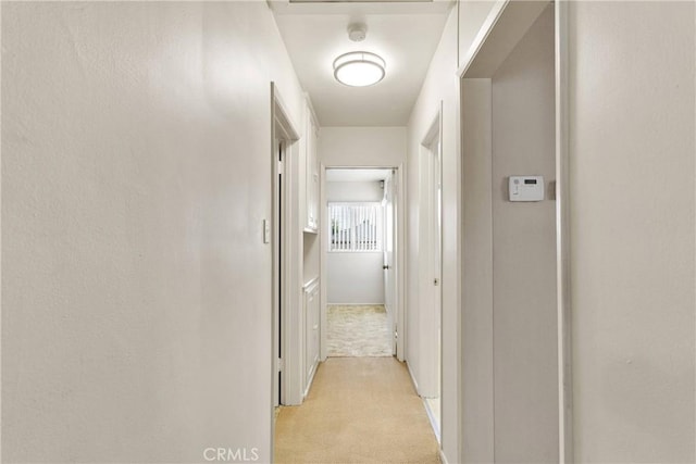 hallway featuring baseboards and light carpet