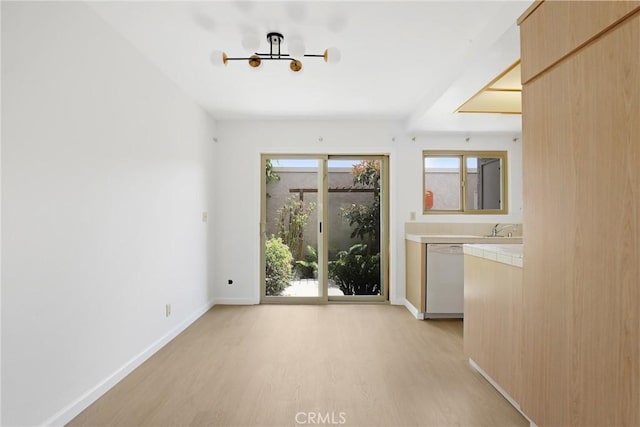 unfurnished dining area with a sink, baseboards, light wood-style flooring, and a chandelier