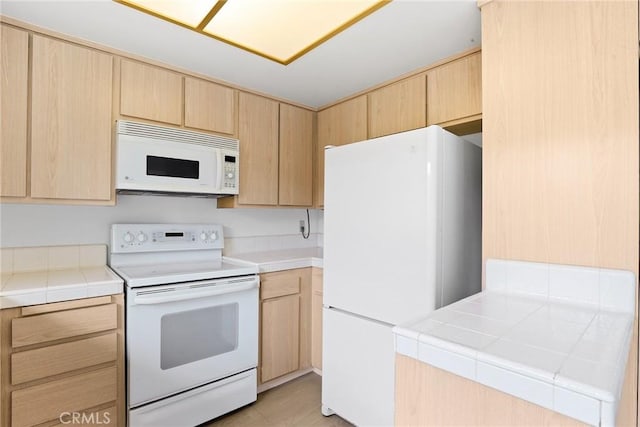 kitchen featuring light brown cabinets, tile countertops, and white appliances