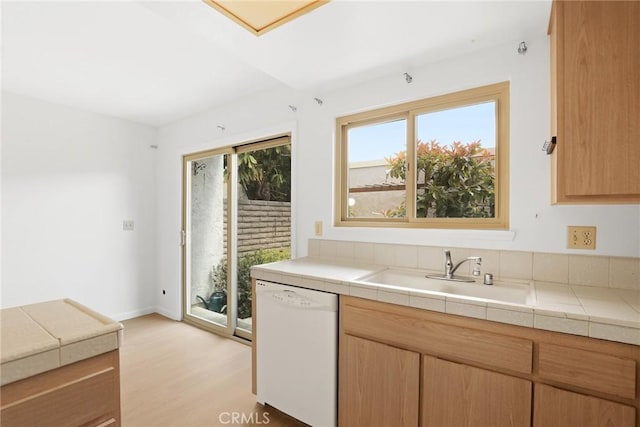 kitchen featuring white dishwasher, tile counters, a sink, and light wood-type flooring