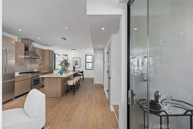 kitchen with a kitchen breakfast bar, high end appliances, modern cabinets, and wall chimney exhaust hood