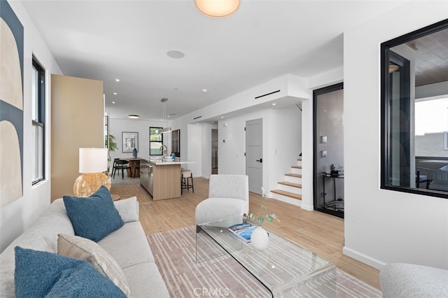 living room with stairway, baseboards, and light wood-type flooring