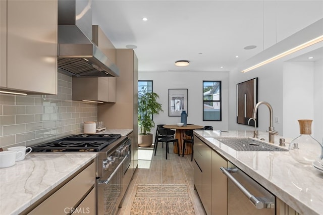 kitchen featuring decorative backsplash, light stone countertops, wall chimney range hood, a sink, and stainless steel appliances