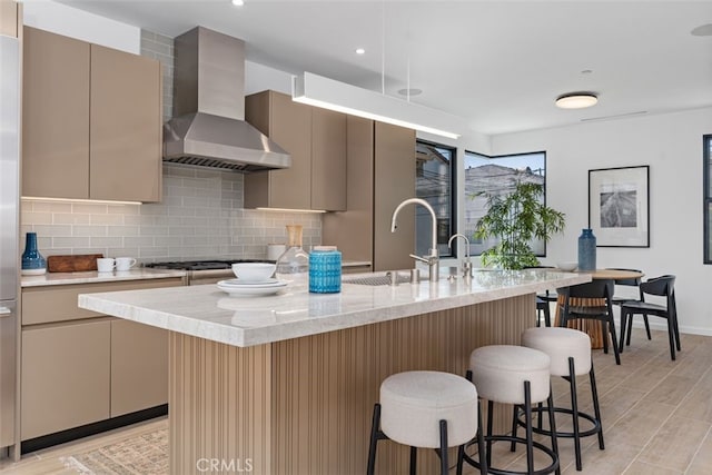 kitchen with a breakfast bar area, wall chimney range hood, gas cooktop, tasteful backsplash, and a sink