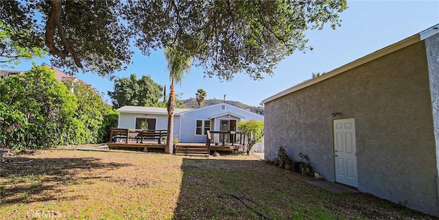 back of property featuring a lawn, a wooden deck, and stucco siding