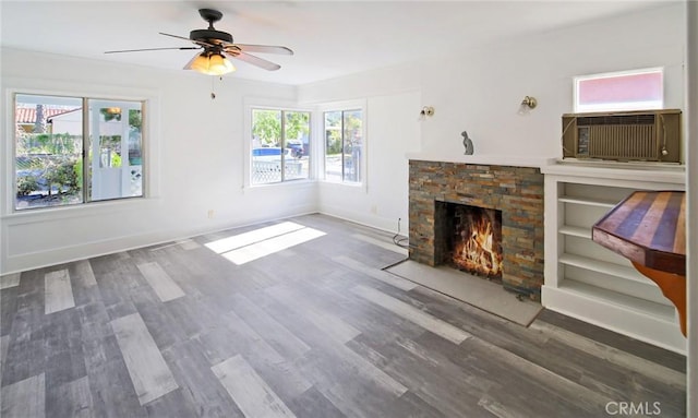 unfurnished living room featuring baseboards, a ceiling fan, a stone fireplace, and wood finished floors