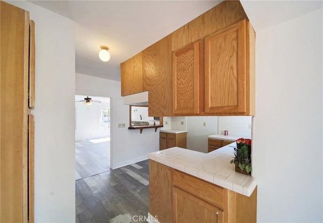 kitchen with baseboards, tile counters, tasteful backsplash, a ceiling fan, and dark wood finished floors