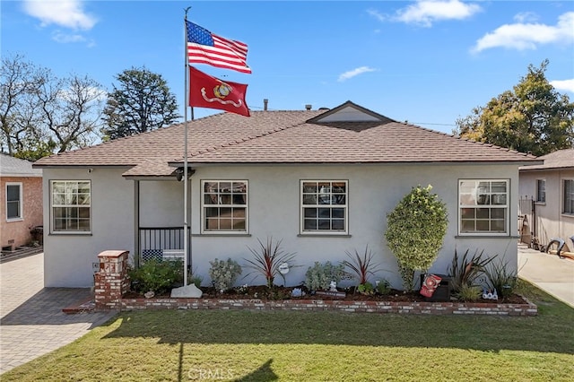view of front facade featuring a shingled roof, stucco siding, and a front yard