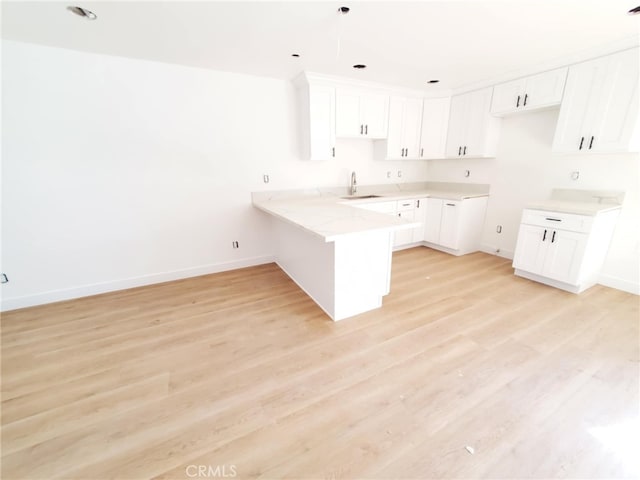kitchen featuring a sink, baseboards, light wood-type flooring, and a peninsula