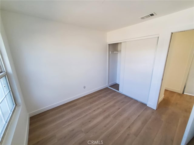 unfurnished bedroom featuring visible vents, baseboards, wood finished floors, and a closet