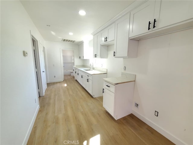kitchen featuring visible vents, light wood-type flooring, a sink, baseboards, and white cabinetry