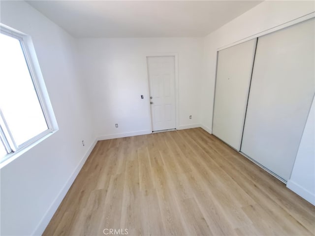unfurnished bedroom with baseboards, multiple windows, and light wood finished floors