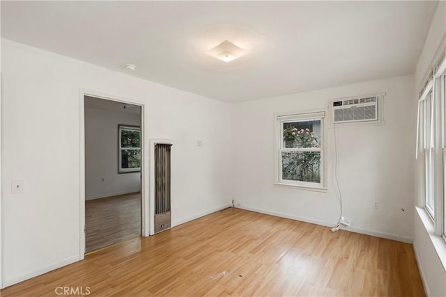 unfurnished room featuring a wealth of natural light, light wood finished floors, and a wall mounted air conditioner