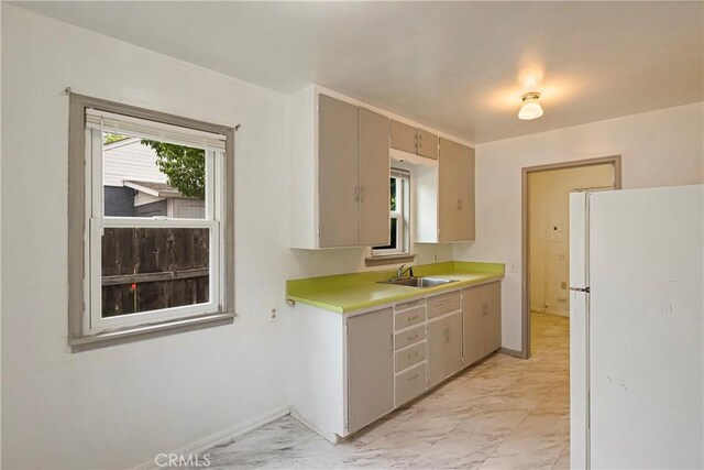 kitchen with plenty of natural light, a sink, light countertops, freestanding refrigerator, and marble finish floor