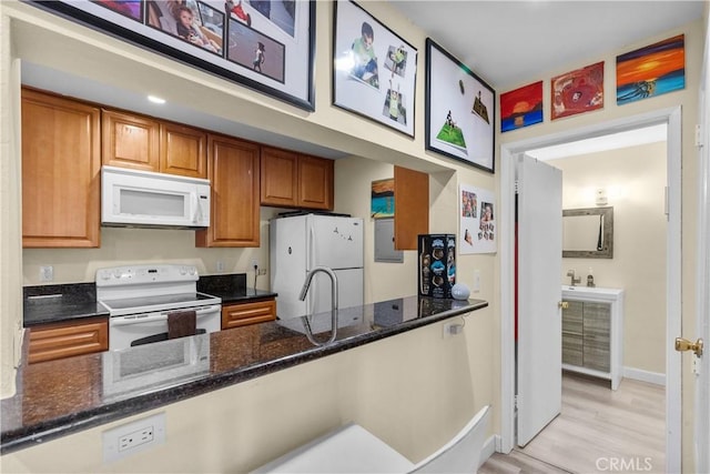 kitchen featuring white appliances, brown cabinets, dark stone countertops, and light wood-style floors