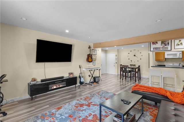 living room featuring light wood-style floors, baseboards, a glass covered fireplace, and recessed lighting