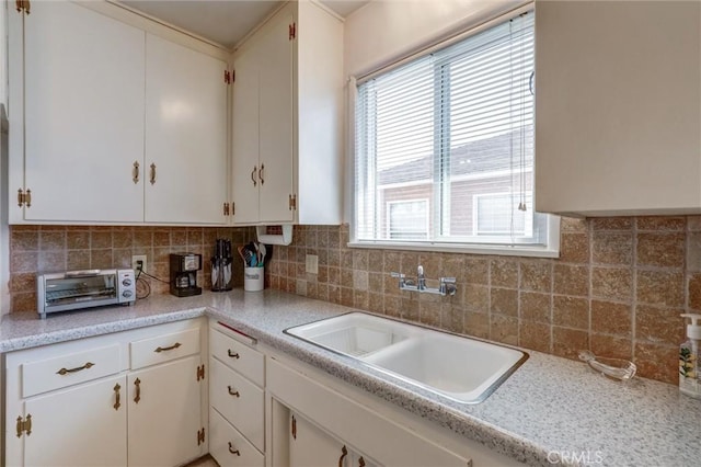 kitchen with a sink, light countertops, a toaster, white cabinetry, and tasteful backsplash