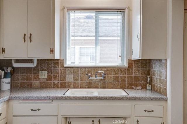 kitchen featuring a sink, backsplash, white cabinets, and light countertops