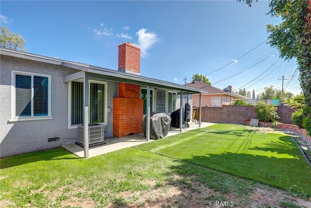 back of property with central AC, fence, stucco siding, a chimney, and a lawn