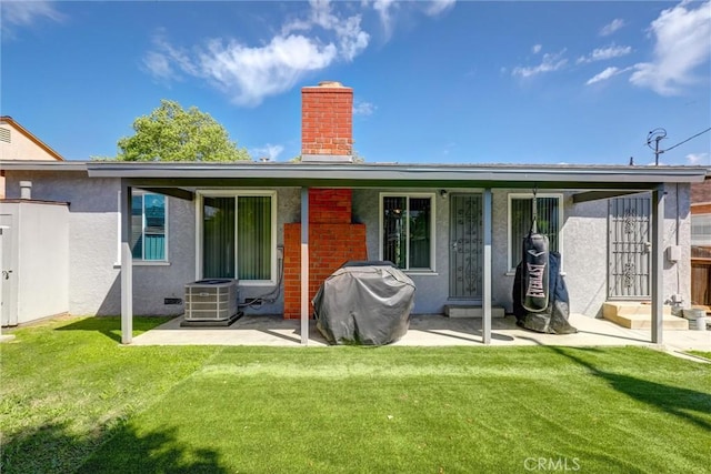 back of property with a lawn, a chimney, cooling unit, and stucco siding