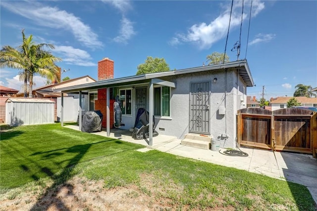 back of house featuring fence, stucco siding, a yard, a chimney, and a storage shed