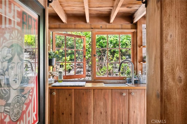 interior details with a sink, wood ceiling, beamed ceiling, and wooden walls