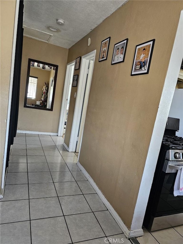 hallway featuring a textured ceiling, baseboards, light tile patterned floors, and attic access