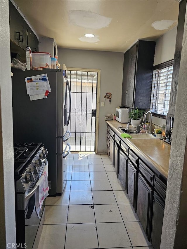 kitchen with light tile patterned flooring, a sink, dark cabinetry, white microwave, and range with gas cooktop