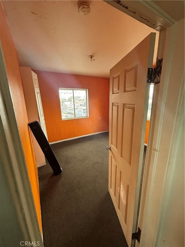 hallway with baseboards and dark colored carpet