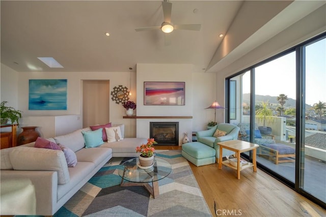 living room with vaulted ceiling, a glass covered fireplace, a wealth of natural light, and light wood-style floors