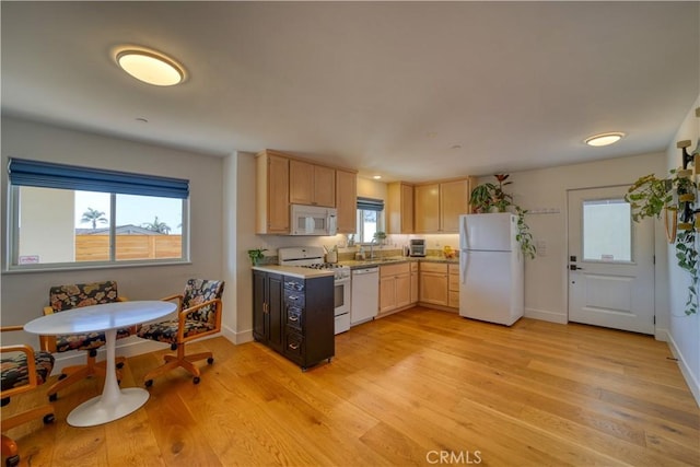 kitchen with light brown cabinets, white appliances, light countertops, a sink, and light wood-style flooring