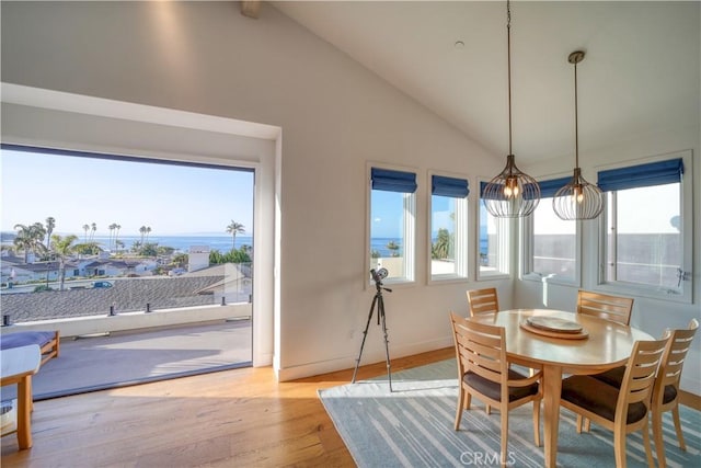 dining area with baseboards, a water view, wood finished floors, and vaulted ceiling