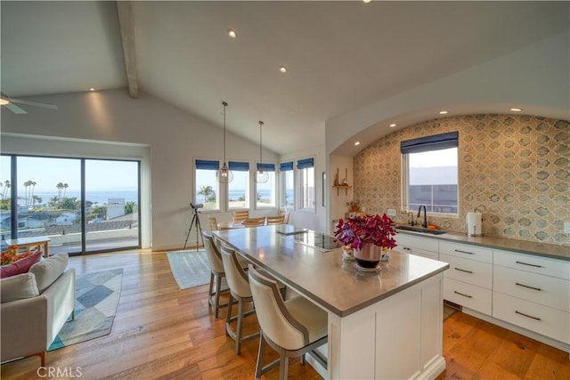 kitchen with light wood-style floors, open floor plan, a center island, white cabinetry, and lofted ceiling with beams