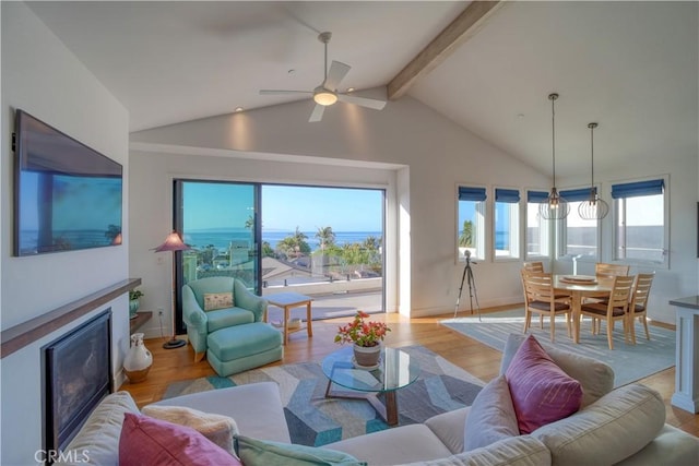 living area featuring lofted ceiling with beams, a glass covered fireplace, wood finished floors, and ceiling fan