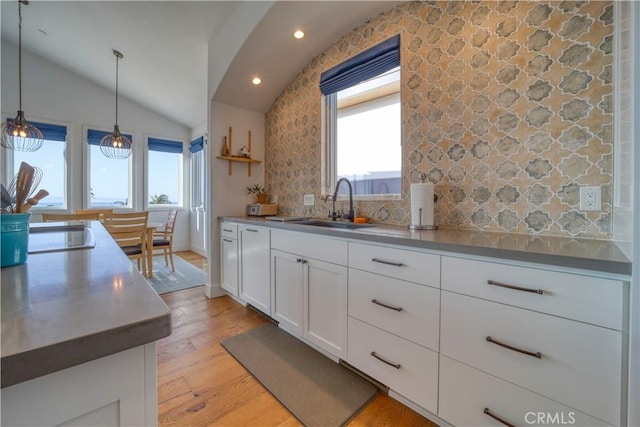 kitchen featuring white cabinets, a sink, light wood-style flooring, backsplash, and vaulted ceiling